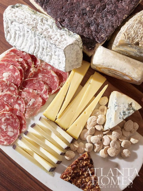 Cheese board with salami, various cheeses, nuts, and a piece of nut brittle.