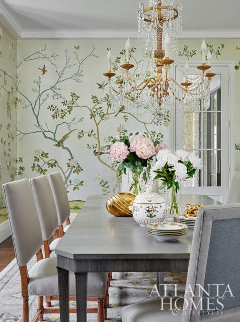 Dining room with Chinoiserie wallpaper, upholstered chairs, and a crystal chandelier.