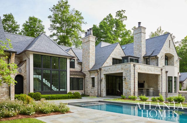 Stone mansion with slate roof, large windows, and swimming pool. Atlanta Homes & Lifestyles logo in