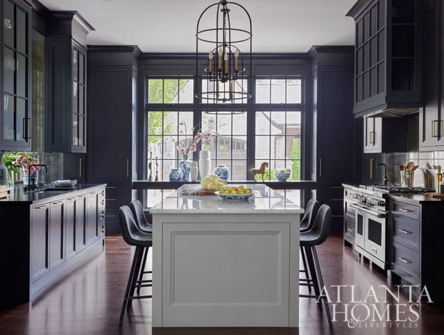 Dark blue kitchen with marble island, stainless steel range, and brass hardware.