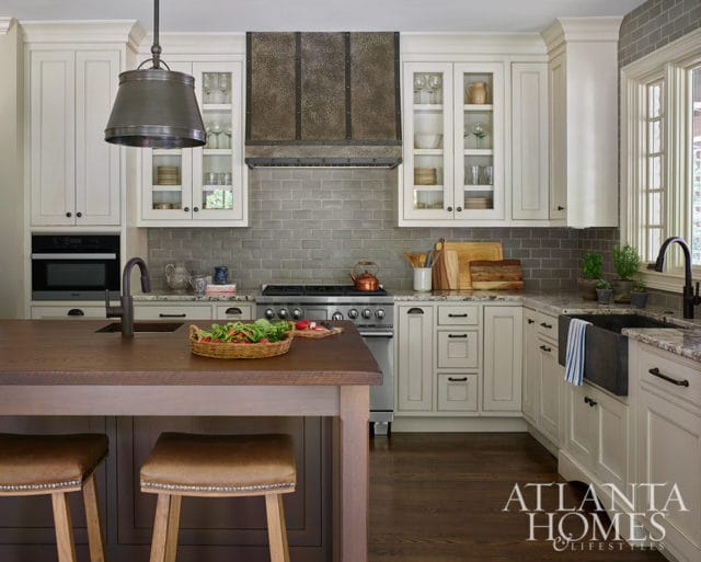 Cream kitchen with gray subway tile backsplash, dark wood island, and metal range hood.