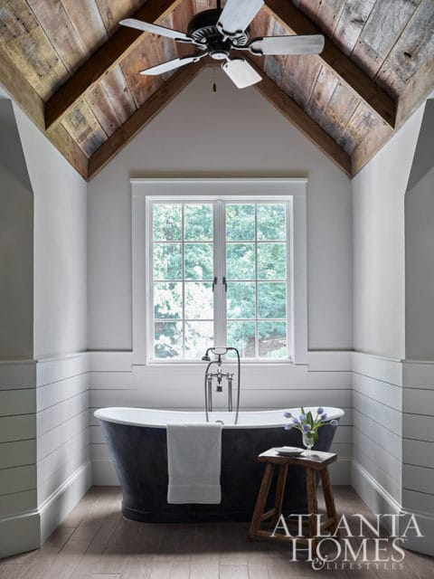 Bathroom with dark clawfoot tub, shiplap walls, wood ceiling, and window overlooking trees.