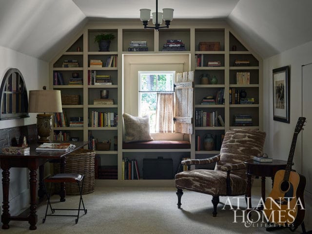 Study with built-in bookshelves, window seat, patterned armchair, and guitar