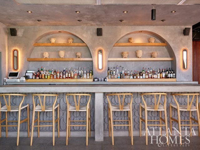 Bar with concrete counter, wooden stools, and shelves stocked with liquor bottles.