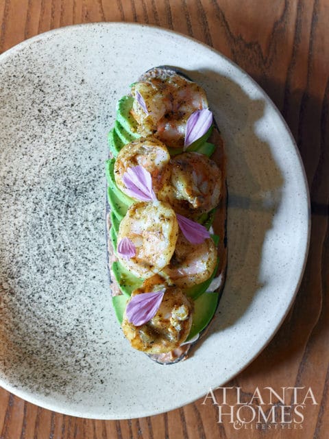 Shrimp and avocado toast on a speckled plate with purple flower petals