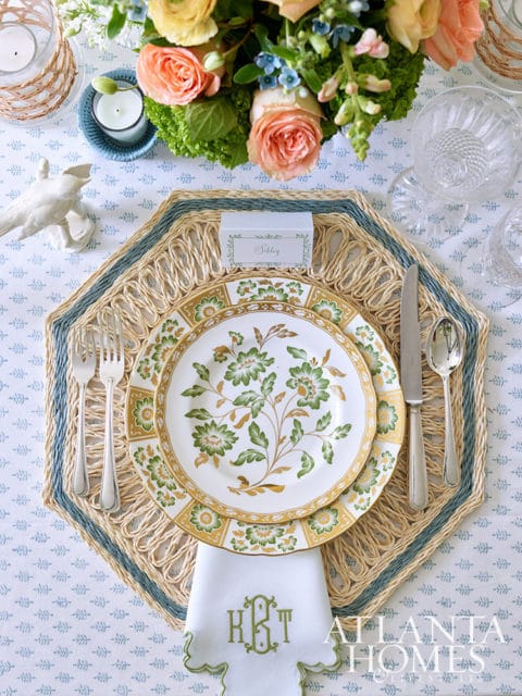 Table setting with floral china, woven placemat, monogrammed napkin, and floral centerpiece.