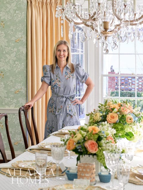 Woman in floral dress standing by dining table with floral arrangements and crystal chandelier