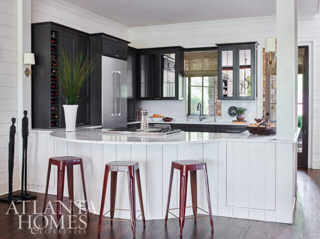 Dark gray kitchen cabinets, stainless steel refrigerator, and marble island with red stools