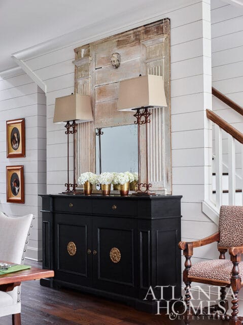 Black sideboard with ornate gold hardware, topped with lamps and hydrangeas.