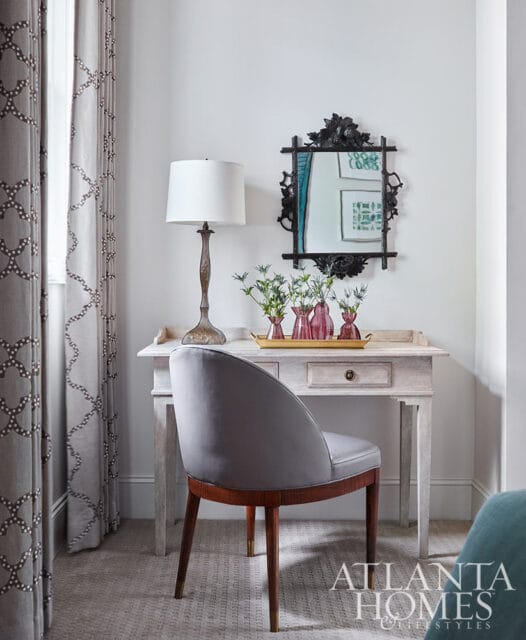 Gray upholstered chair at a light wood desk with pink vases and a lamp.