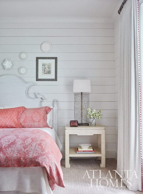 Bedroom with shiplap walls, white headboard, coral patterned bedding, and a bedside table with a