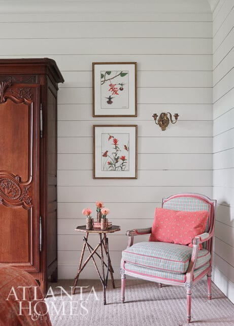 Armoire, chair with plaid upholstery, and botanical prints on shiplap walls.