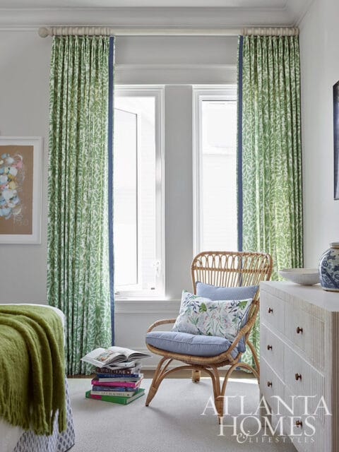 Bedroom with green floral curtains, wicker chair with blue striped cushions, and white dresser