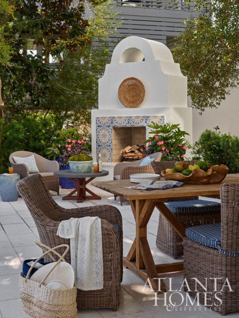 Outdoor patio with wicker furniture, wooden dining table, and white fireplace with blue tile