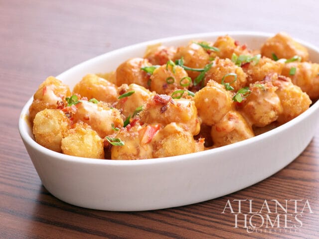 Tater tots topped with cheese sauce, bacon bits, and chives in a white oval bowl