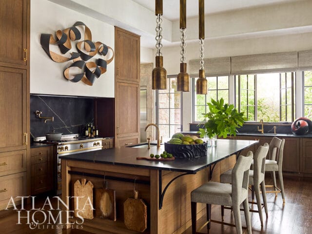 Kitchen with wood cabinetry, black marble backsplash, and island with bar stools.