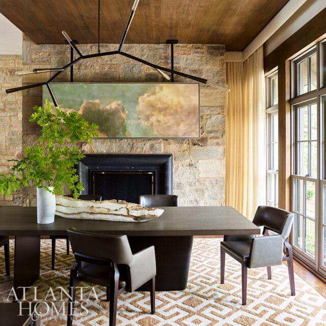 Dining room with stone fireplace, abstract painting, and dark wood table.