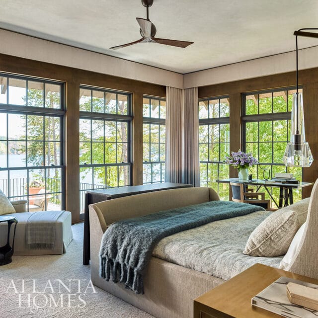 Bedroom with large windows overlooking a lake, a daybed with a teal throw, and a ceiling fan.