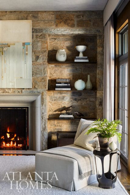 Living room with stone fireplace, built-in shelves with decor, and chaise lounge.