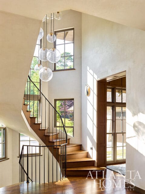Curved wooden staircase with black railing and globe pendant lights.