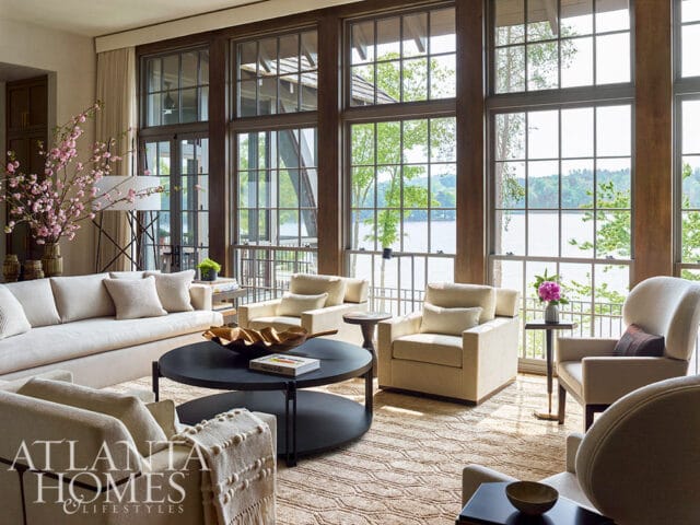Living room with large windows overlooking a lake, neutral-toned furniture, and a dark coffee table.
