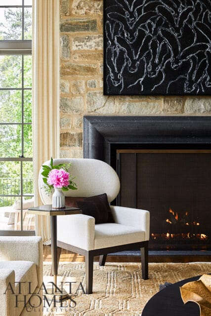 Living room with stone fireplace, white armchair, and pink peonies on side table.