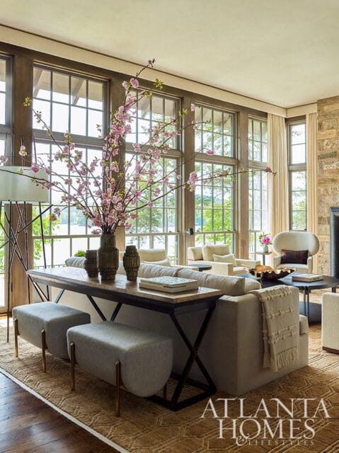 Living room with large windows, neutral sofa, console table with floral arrangement, and stone