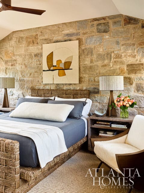 Bedroom with stone wall, woven headboard, blue bedding, and abstract art.