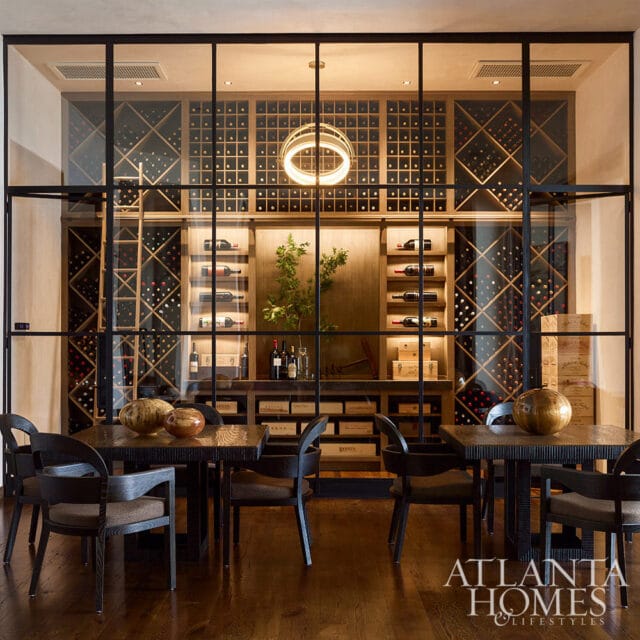 Wine cellar with glass walls, dark wood tables, chairs, and extensive wine racks.