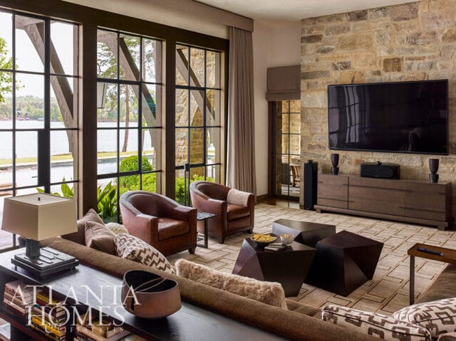 Living room with stone accent wall, leather chairs, and large windows overlooking a lake.