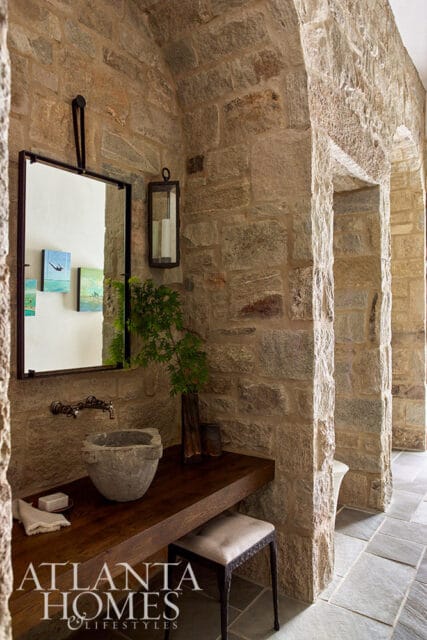 Stone bathroom with wooden vanity, stone basin sink, and metal stool.