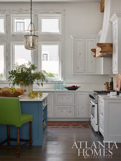 White kitchen with blue island, green stool, and distressed cabinetry.