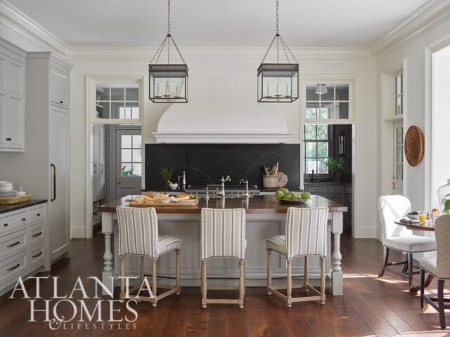 Kitchen with island, striped bar stools, black marble backsplash, and pendant lights.