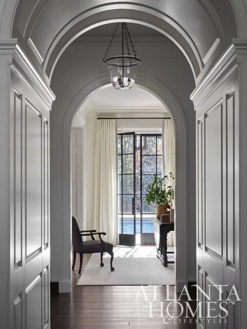 Hallway with arched doorway, paneled walls, dark wood floors, and a glass lantern pendant light.