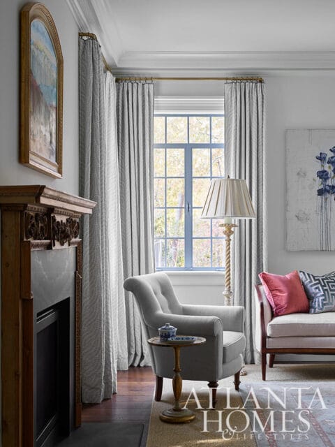 Gray armchair next to a fireplace, with patterned curtains and a window view.