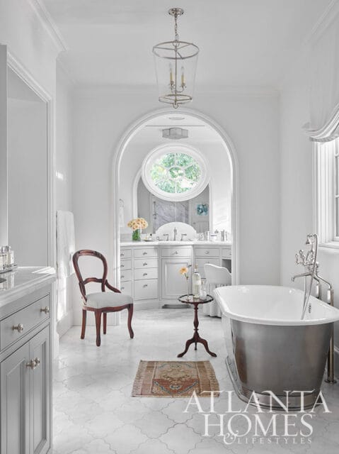 White bathroom with freestanding tub, arched doorway, circular window, and vanity