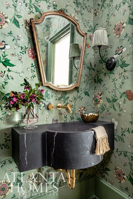 Powder room with floral wallpaper, black marble vanity, gold faucet, and ornate mirror.