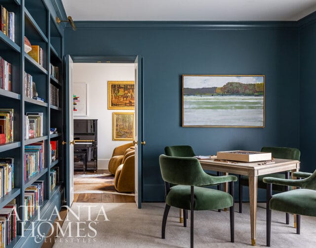 Dark blue room with built-in bookshelves, a game table with green velvet chairs, and a landscape