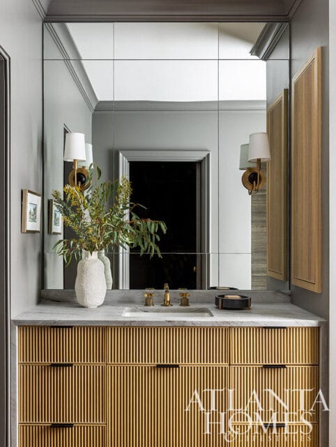 Bathroom vanity with fluted gold drawers, marble countertop, and large mirrored wall