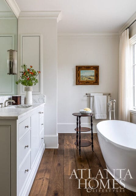 White bathroom vanity with marble countertop, freestanding tub, and dark wood floors.