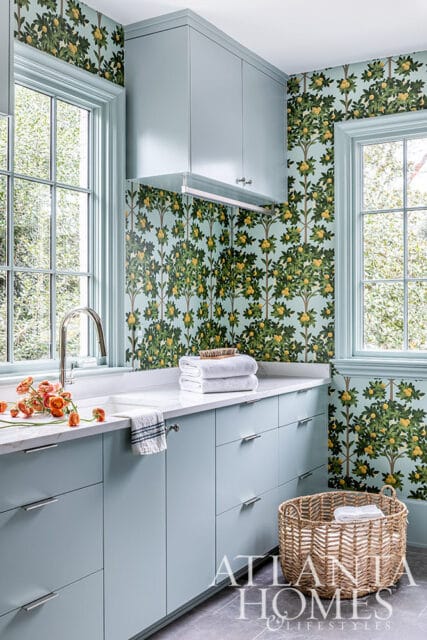 Light blue laundry room cabinets with white marble countertop and fruit tree wallpaper.