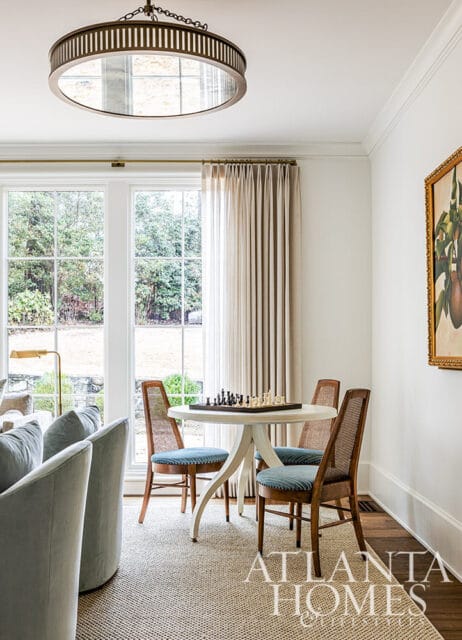 Round table with chess set, cane-back chairs, and large windows overlooking garden