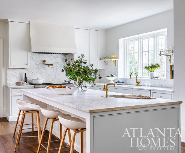 White kitchen with marble island, brass fixtures, and white cabinetry.
