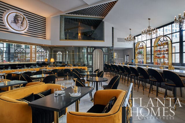 Restaurant dining room with gold velvet booths, black chairs, and a long bar with liquor shelves.