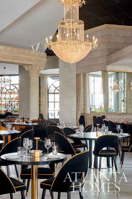 Restaurant dining room with black and gold chairs, round tables, and a crystal chandelier.