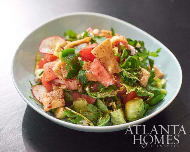 Salad with tomatoes, radishes, pita bread, and herbs in a light blue bowl.