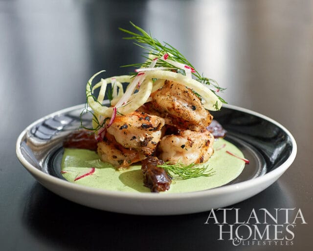 Grilled shrimp with green sauce, shaved fennel, and dill garnish on a black and white plate.