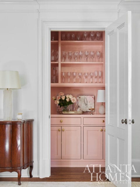 Pink built-in cabinetry with glass shelves displaying glassware.