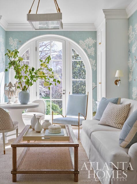Light blue living room with floral wallpaper, arched window, white sofa, and cane coffee table.