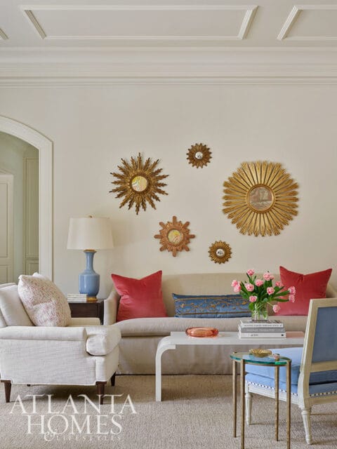Living room with a beige sofa, red pillows, sunburst mirrors, and a white coffee table.